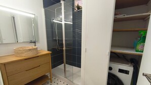 A bathroom with a glass shower enclosure, a wooden vanity with a sink, and a washing machine. - Apartment with sea view - 4 guests (Argelès-sur-Mer)