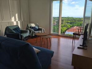 A living room with a large window, a sofa, two armchairs, a small table, and a TV. - Apartment with sea view - 4 guests (Argelès-sur-Mer)