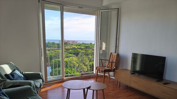A living room with a sofa, a TV, a wooden cabinet, and a balcony with a view of greenery and buildings. - Apartment with sea view - 4 guests (Argelès-sur-Mer)