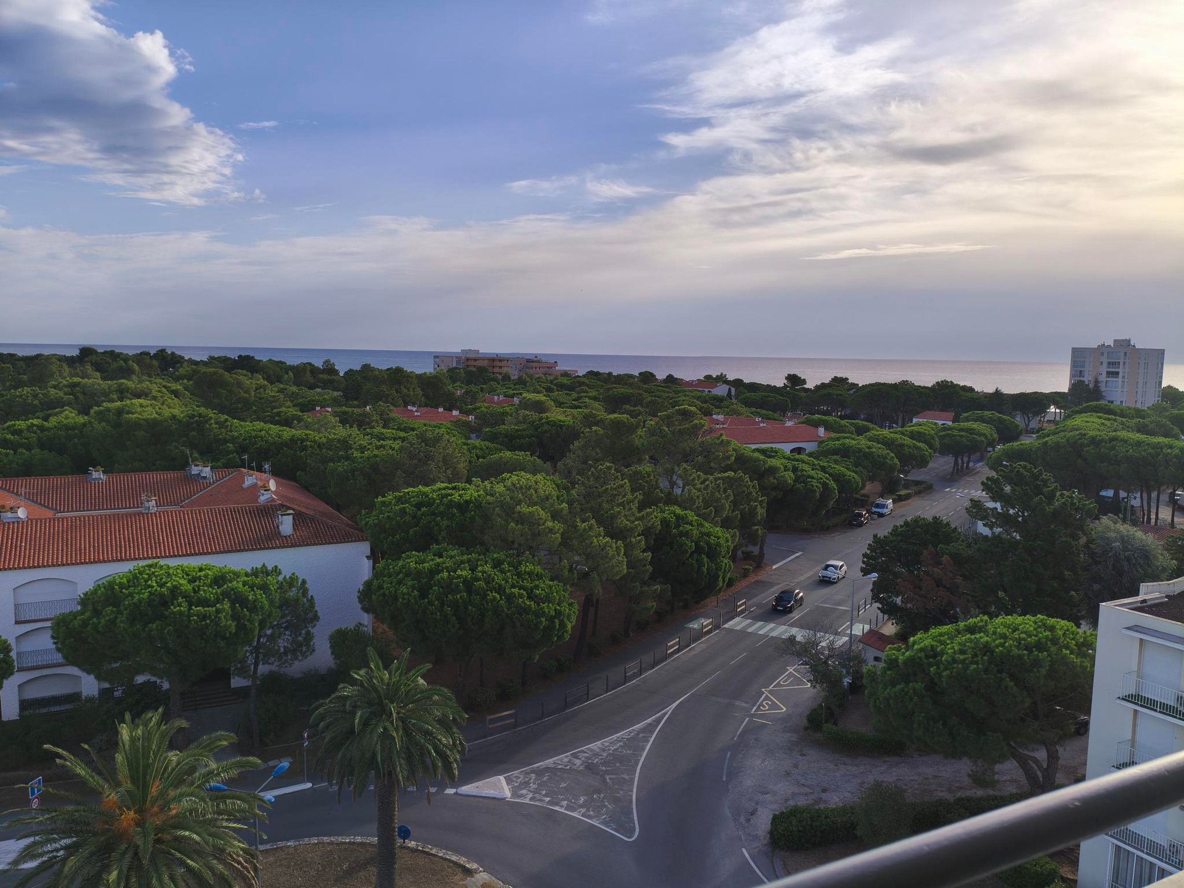 Eine Küstenwohngegend mit einer Straße, die zu einem Strand führt, umgeben von üppiger Vegetation und Gebäuden mit roten Ziegeldächern.