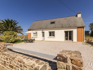 A two-story house with a gravel driveway, a stone wall, and a palm tree in the background.