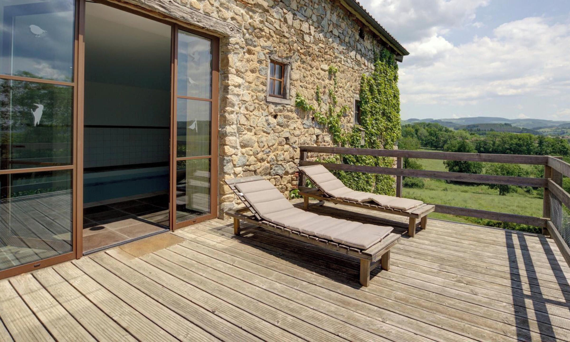 Una terraza de madera con dos sillas reclinables y un ventanal que da a una habitación.