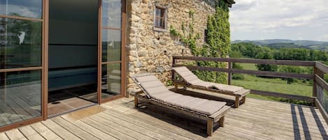 Une terrasse en bois avec deux chaises longues et une porte vitrée donnant sur une pièce.