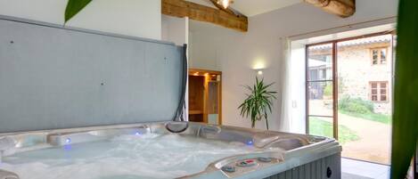 A hot tub with controls, a wooden ceiling beam, a potted plant, and a view of a stone building outside.