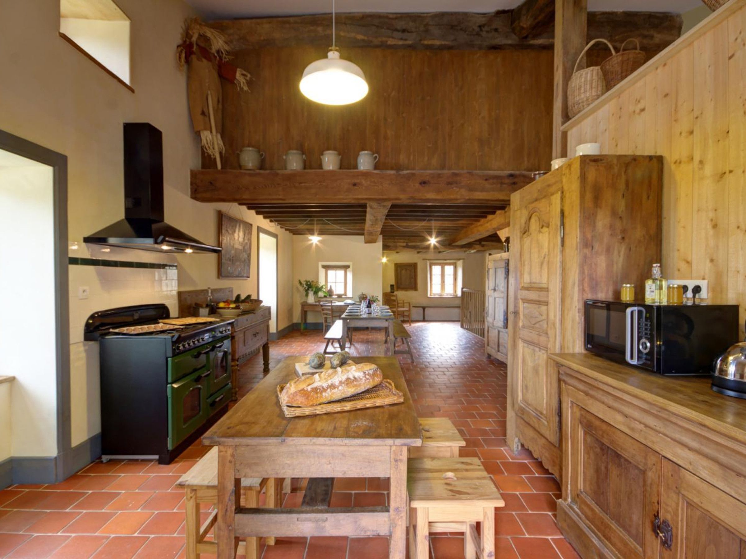 A rustic kitchen with a wooden table, a stove, and a hanging light fixture.