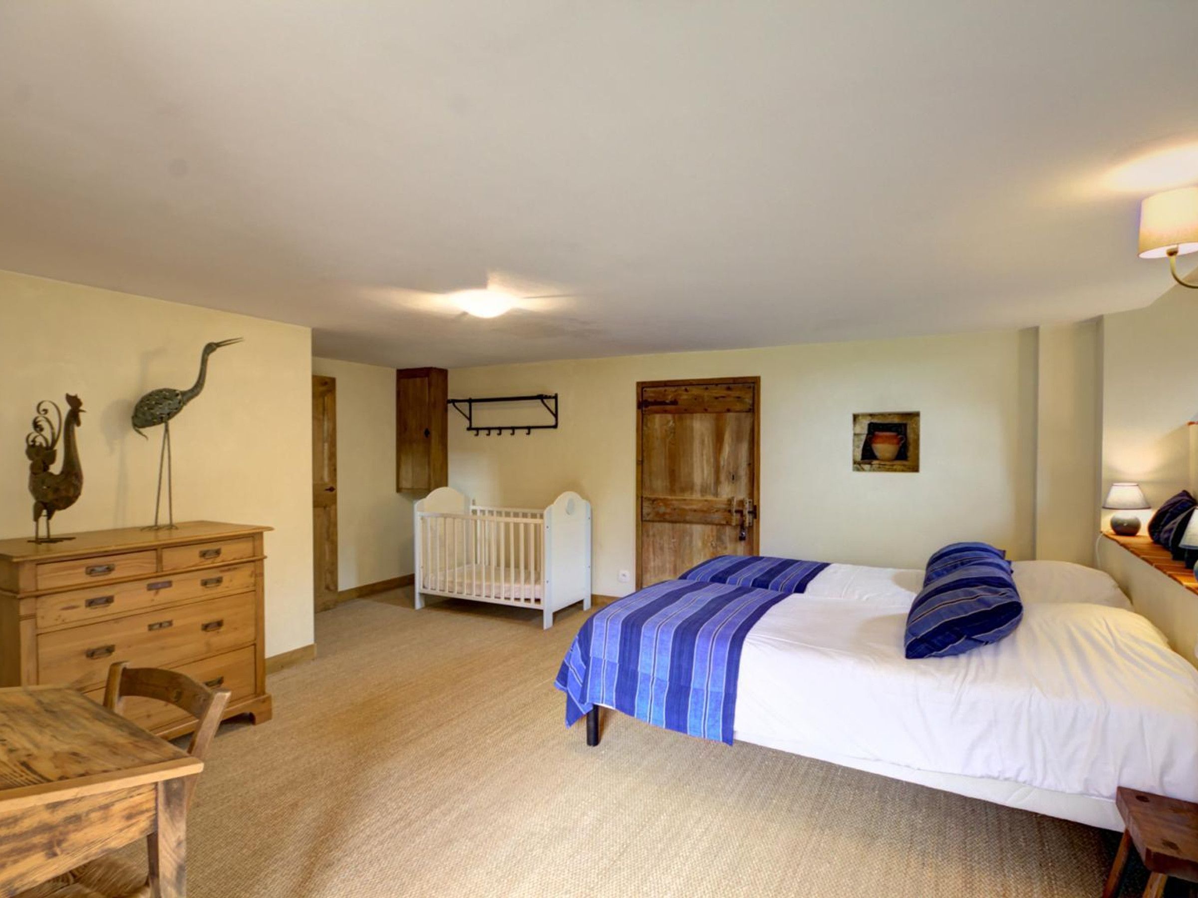 A bedroom with a bed, a wooden dresser, a crib, and a dining table.