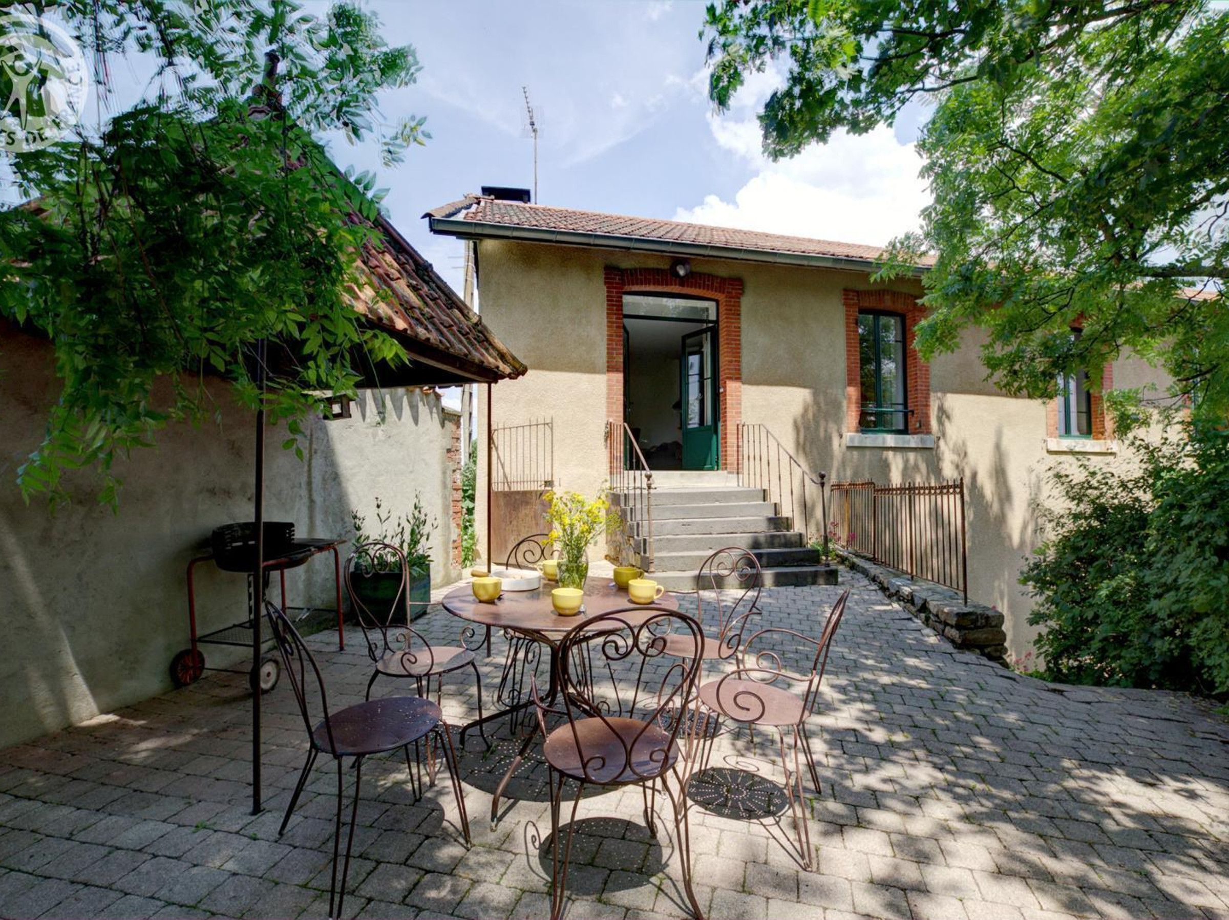 A patio with a table and chairs, a small building with a door, and steps leading to a higher level.