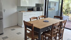 A dining area with a wooden table and chairs, a kitchen with white cabinets, and a sliding glass door leading to an outdoor area. - House with garden - Fouras - 6 guests (Fouras)