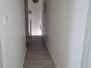 Un pasillo estrecho con suelo de madera, paredes blancas y una puerta al final.