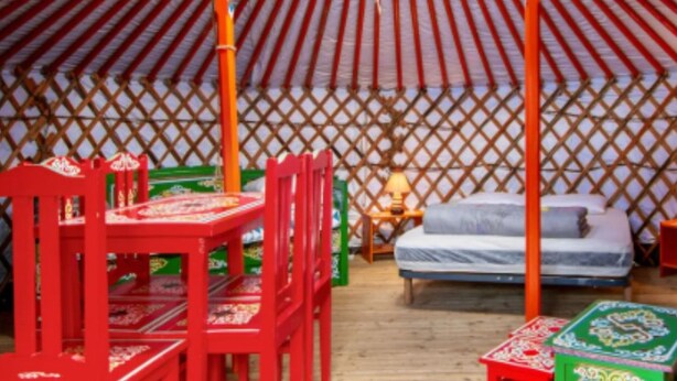 Ein traditionelles Jurten-Interieur mit Bett, Sitzgelegenheit und Tisch.