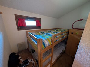 A bunk bed with a striped bedspread, a window with red curtains, a wooden wardrobe, and a desk with a computer and charger. - Ski-in/ski-out duplex, pets welcome - 6 guests (Montgenèvre)