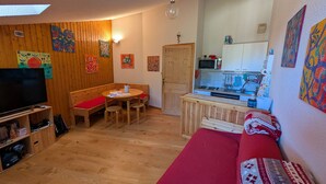 Une pièce chaleureuse avec un plancher en bois, un canapé rouge, un banc en bois, une télévision et un coin cuisine équipé d’un four à micro-ondes et d’un évier.
