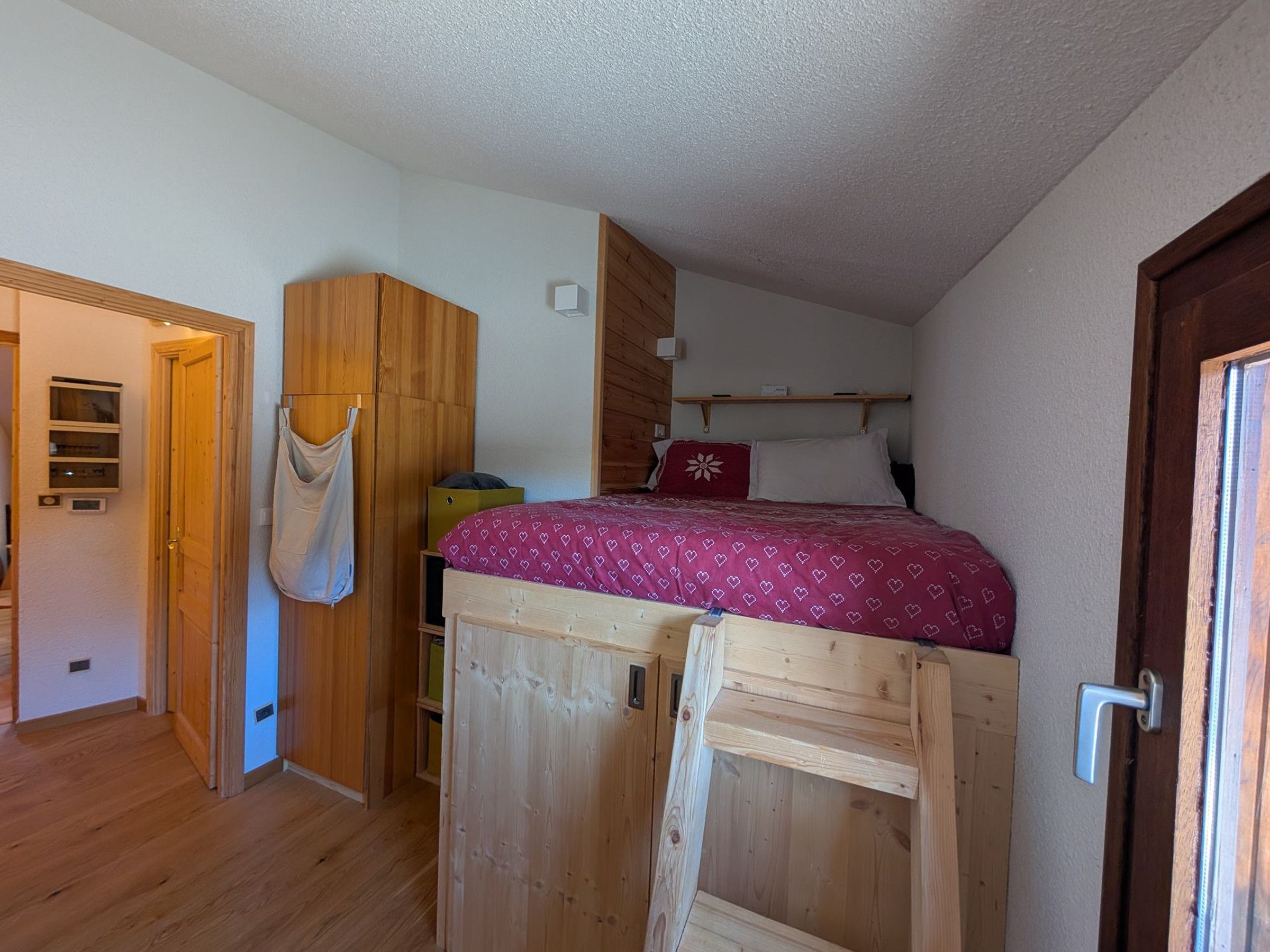 Une chambre avec un lit superposé, une armoire en bois et une porte dotée d’une poignée.