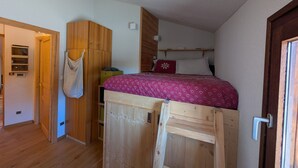 Une chambre avec un lit superposé, une armoire en bois et une porte dotée d’une poignée.