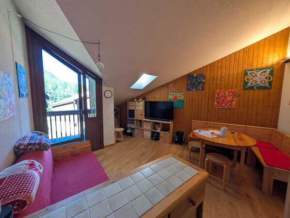 A cozy room with a wooden floor, a dining table, a sofa, and a television. - Ski-in/ski-out duplex, pets welcome - 6 guests (Montgenèvre)