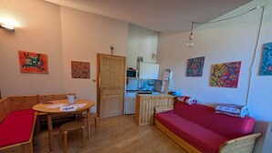 Un espace de vie compact doté d’un plancher en bois, d’un canapé rouge, d’une table à manger en bois avec des chaises, d’un coin cuisine et de diverses œuvres d’art accrochées aux murs.