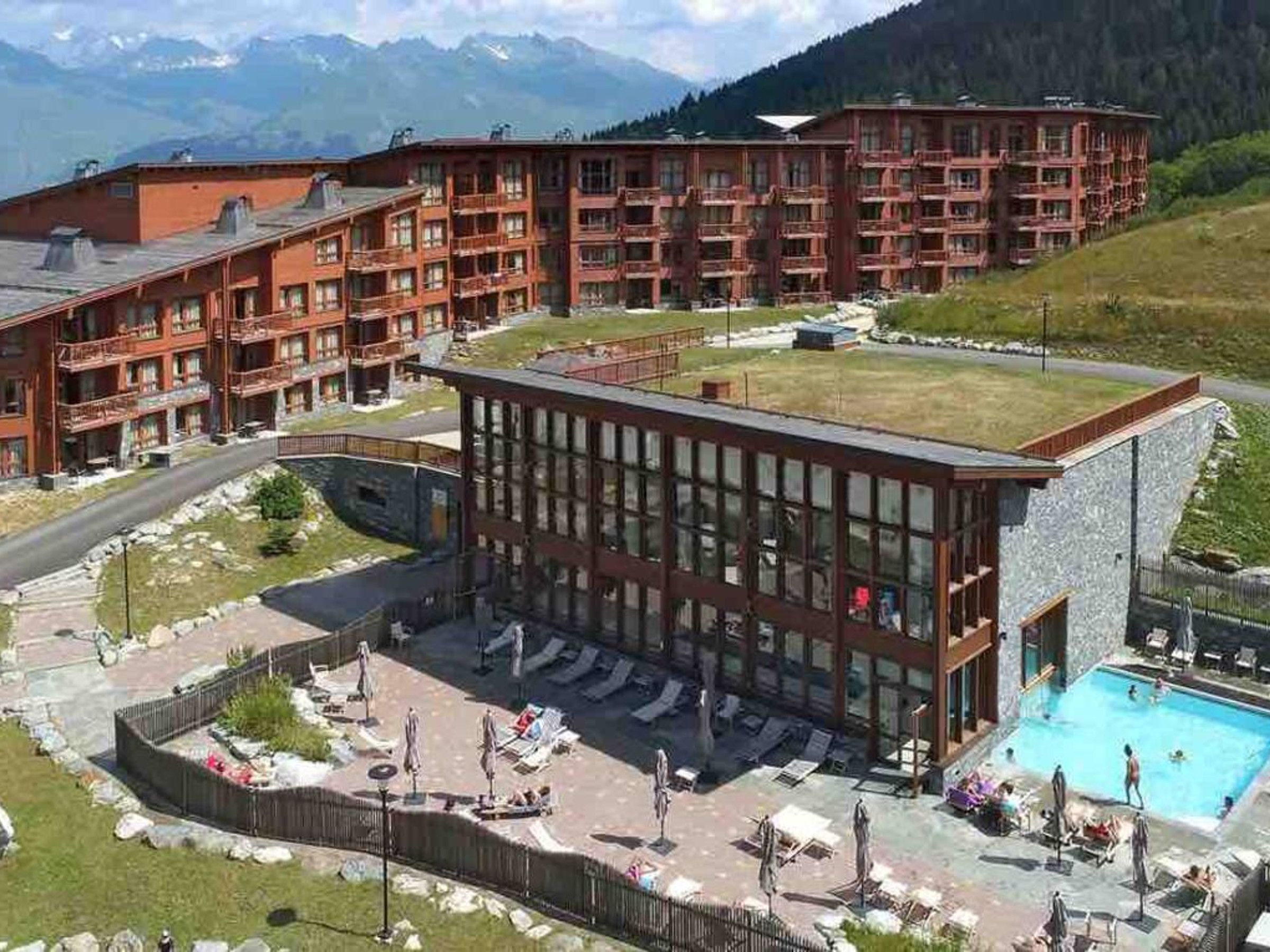 A hotel with multiple floors, a swimming pool, and a mountainous backdrop.