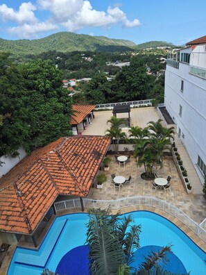 A rooftop pool area with a view of a mountainous landscape, a covered patio with outdoor seating, and a building with a white facade. - Itaipu loft penthouse (Niterói)