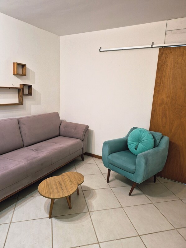 Ein Wohnzimmer mit einer Couch, einem Türkis-Armlehnstuhl, einem Holztisch und Wandregalen.