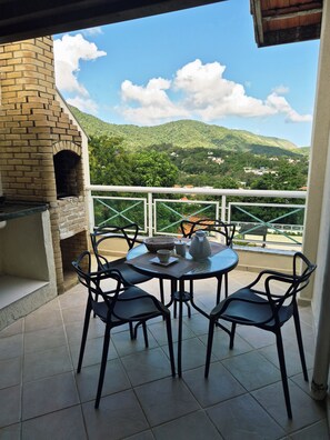 Une terrasse dotée d’un four en briques, d’une table ronde et de chaises, offrant une vue sur un paysage montagneux.