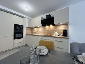 A modern kitchen with built-in appliances, a wooden backsplash, and a dining area with a table set for two. - New and spacious apartment - 4 guests (Briançon)