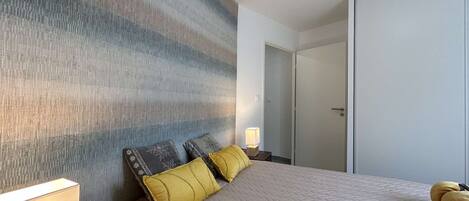 A hotel room with a large bed, a bedside table with a lamp, and a wardrobe.
