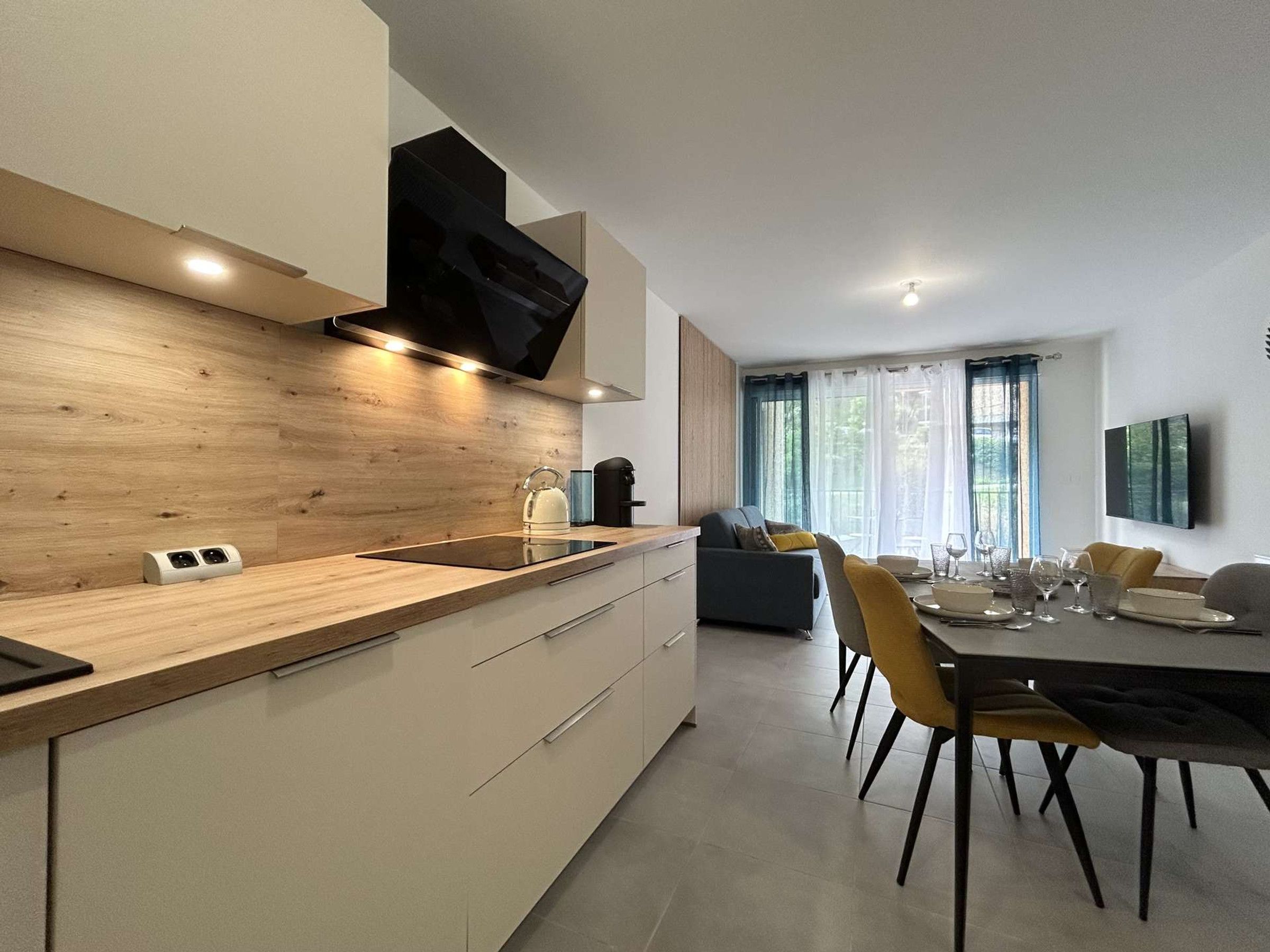 Une cuisine moderne avec un revêtement mural en bois, des appareils électroménagers intégrés et un coin repas avec une table dressée pour quatre personnes.