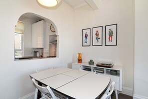 Eine moderne Küche mit weißen Schränken, einem Esstisch mit Stühlen und drei gerahmten Kunstwerken an der Wand.