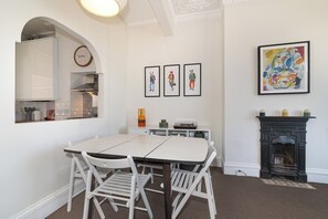 A dining area with a white table and chairs, a kitchen with a clock, framed artwork, and a fireplace. - Charming 2Bed Flat in the Heart of Brixton - Pass the Keys (London)