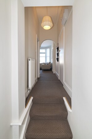 A hallway with a carpeted floor, white walls, a radiator, and a hanging light fixture. - Charming 2Bed Flat in the Heart of Brixton - Pass the Keys (London)
