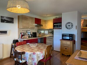 A compact kitchen with wooden cabinets, a microwave, a refrigerator, and a dining table with chairs. - Spacious apartment, mountain view - 4 guests (Pra-Loup)
