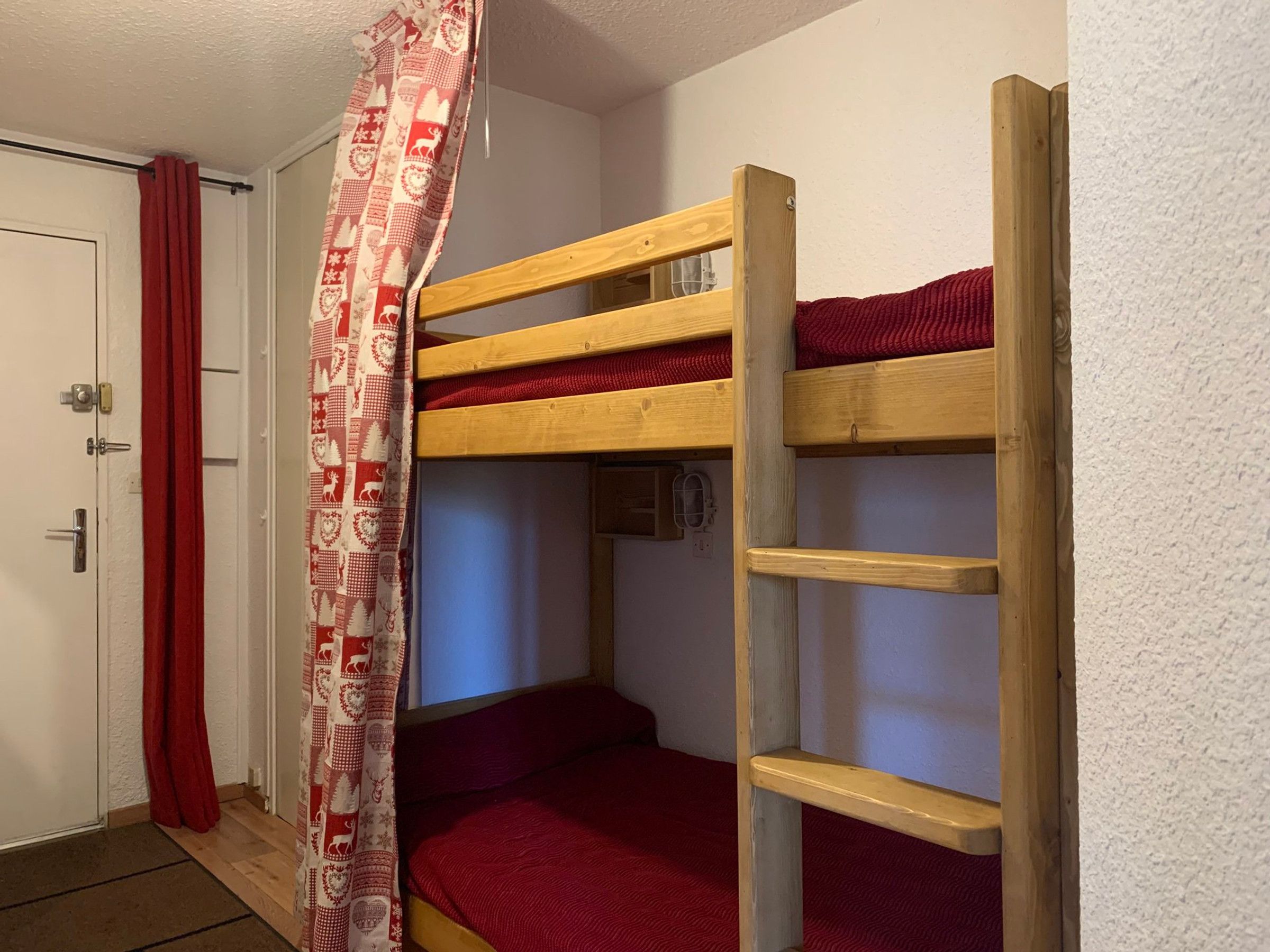 Une chambre avec un lit superposé, une échelle, une porte et un rideau.