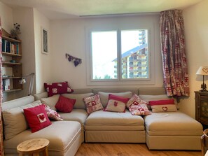 A cozy living room with a sectional sofa, a small round table, and a bookshelf. - Spacious apartment, mountain view - 4 guests (Pra-Loup)