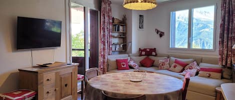 Un salón acogedor con una mesa de comedor redonda, un televisor y un sofá con cojines estampados.