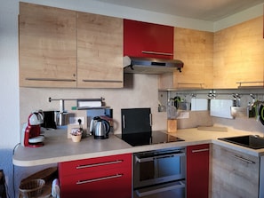 A modern kitchen with wooden cabinets, a red countertop, a built-in oven, and a dishwasher. - Spacious apartment, mountain view - 4 guests (Pra-Loup)