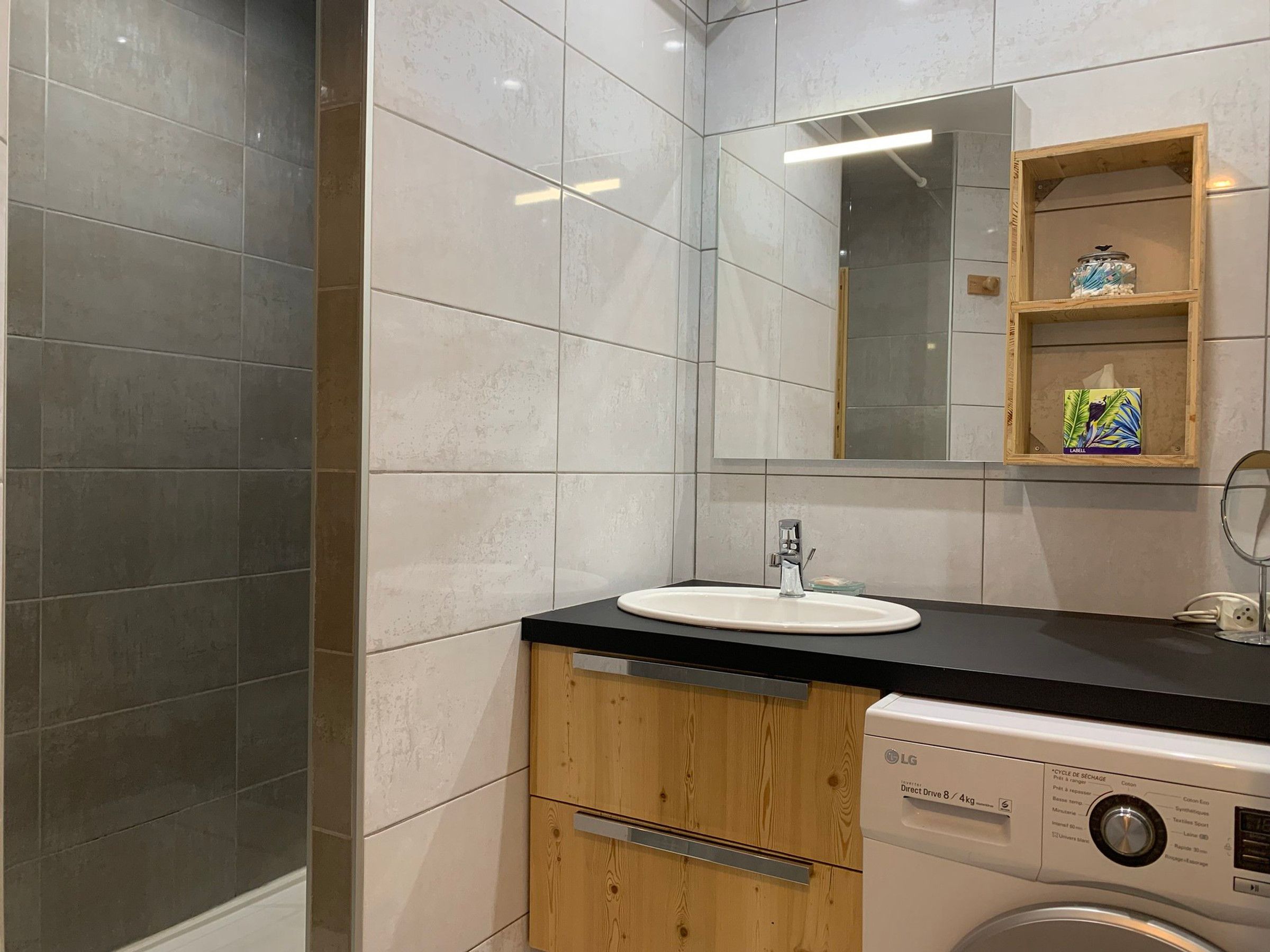 A modern bathroom with a sink, mirror, wooden cabinet, and a washing machine.