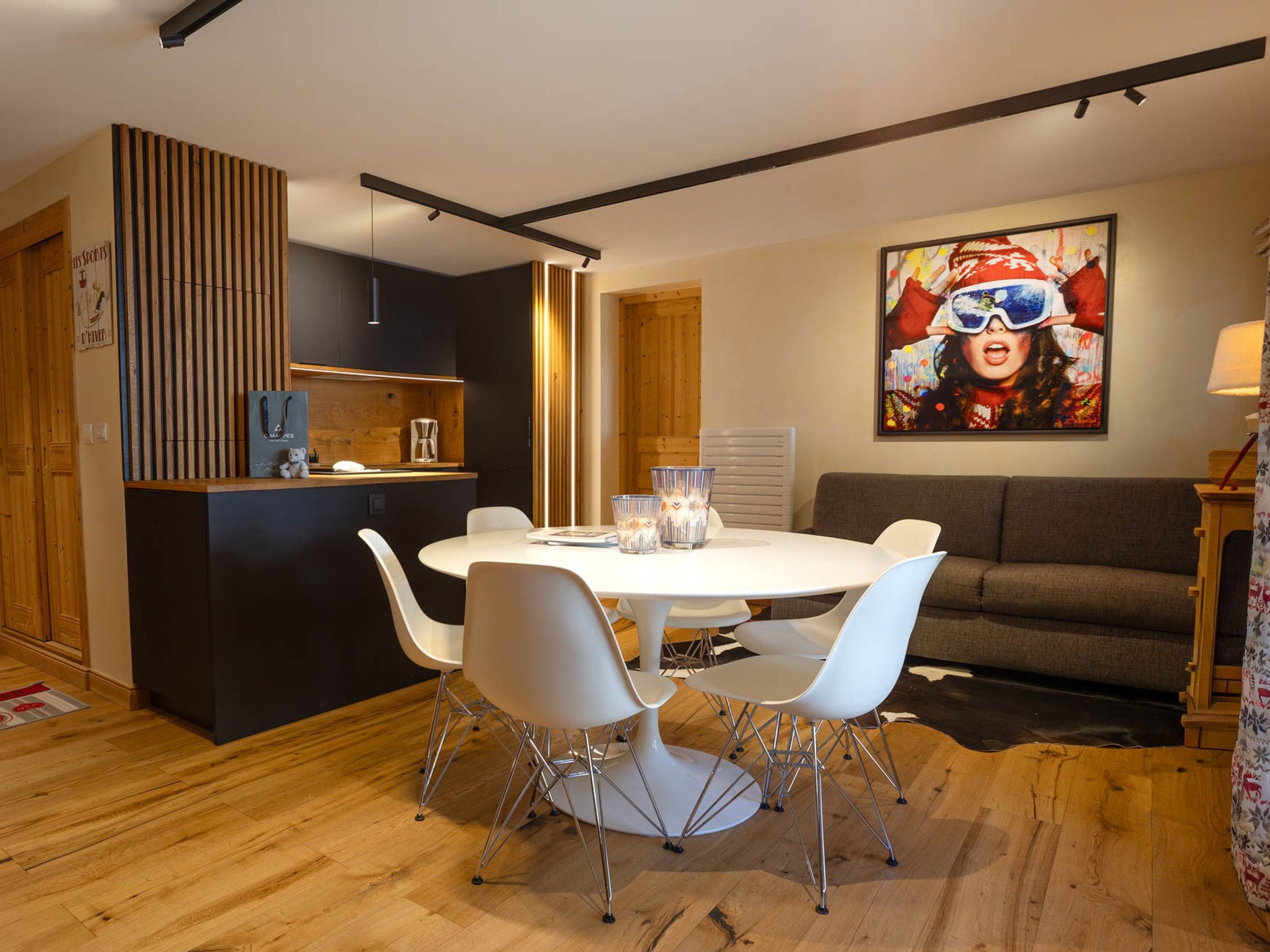 A modern dining area with a round table, white chairs, and a kitchen area with a wooden cabinet and a coffee machine.