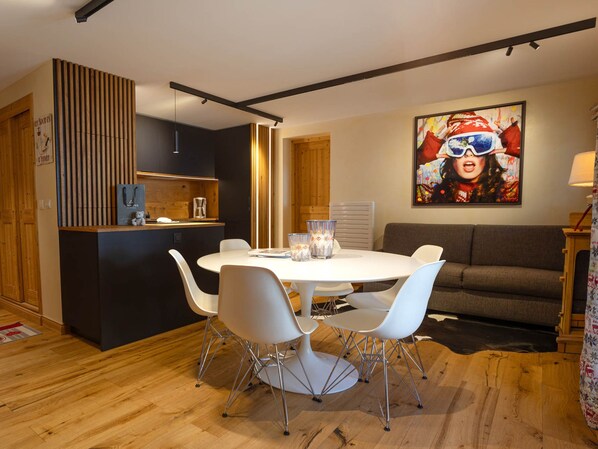 A modern dining area with a round table, white chairs, and a kitchen area with a wooden cabinet and a coffee machine. - Central apartment with large terrace (Les Deux Alpes)