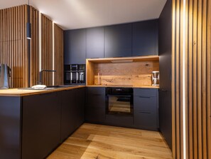 A modern kitchen with dark cabinetry, a wooden countertop, and built-in appliances. - Central apartment with large terrace (Les Deux Alpes)