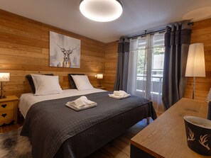 A wooden-paneled bedroom with a bed, two bedside tables, a lamp, a painting, and a window with curtains. - Central apartment with large terrace (Les Deux Alpes)