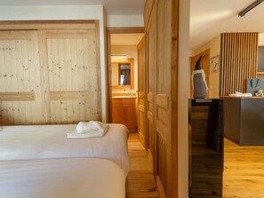 A hotel room with a wooden wardrobe, a bed with a white duvet, a desk with a computer, and a bathroom visible through an open door. - Central apartment with large terrace (Les Deux Alpes)