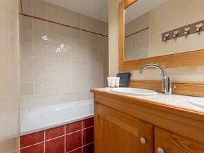 A bathroom with a white bathtub, wooden vanity, and a mirror above the sink. - Central apartment with large terrace (Les Deux Alpes)