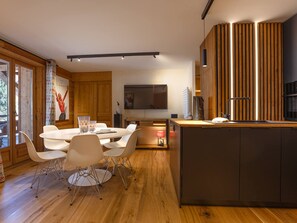 A modern kitchen with a central island, wooden cabinetry, and a dining area with white chairs. - Central apartment with large terrace (Les Deux Alpes)