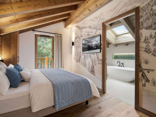 A bedroom with a bed, a window, a wall-mounted picture, and a bathroom with a bathtub. - Chalet at the slopes - 12 guests (Méribel Village)