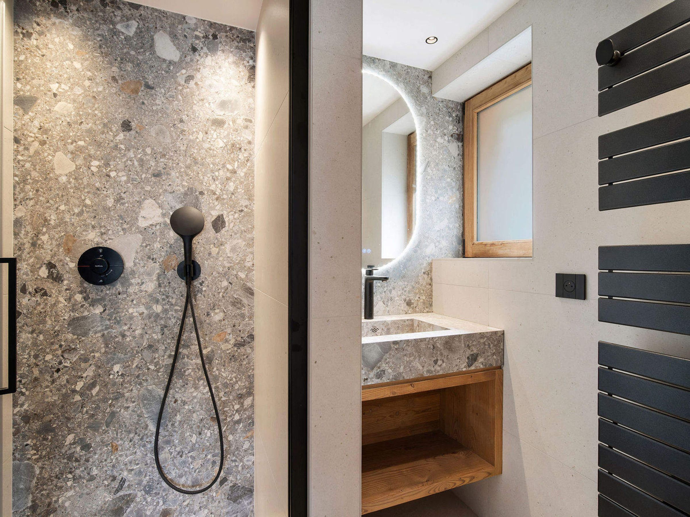 A modern bathroom with a stone wall, a handheld showerhead, a wooden vanity, and a mirror.