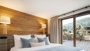 Une chambre avec un grand lit, une tête de lit en bois, deux lampes de chevet et une vue sur un paysage montagneux, visible à travers une porte-fenêtre coulissante.