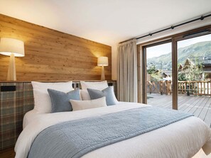 Quarto com cama grande, cabeceira de madeira, duas luminárias de apoio e vista para uma paisagem montanhosa através de uma porta de correr de vidro.