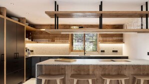 Une cuisine moderne dotée d’un îlot central, de tabourets de bar, de meubles de rangement en bois et d’une fenêtre avec des stores.