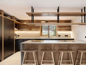 Cozinha moderna com ilha central, banquetas, armários de madeira e janela com persianas.