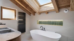Une salle de bain moderne avec une baignoire sur pieds, un plafond en bois et un puits de lumière.